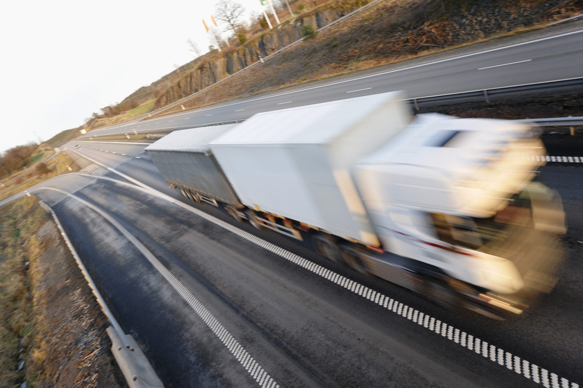 Speedy truck driving. White truck, slightly blurred, driving at great speed on newly laid highway, trademarks removed, red lines are just standards